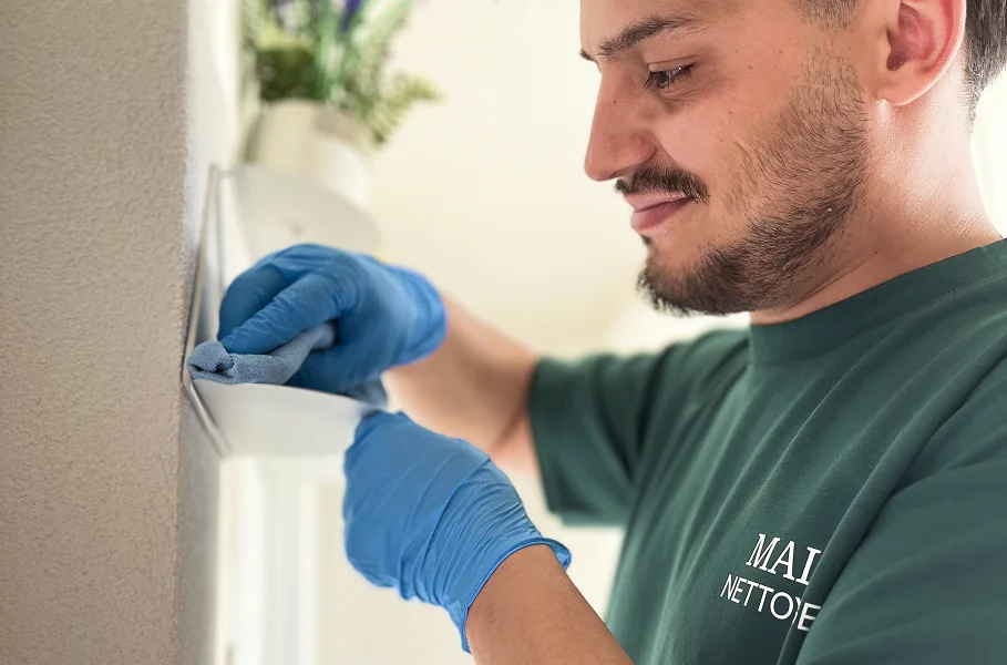 Homme souriant portant un t-shirt Malo Nettoyage nettoyant une surface avec un chiffon microfibre