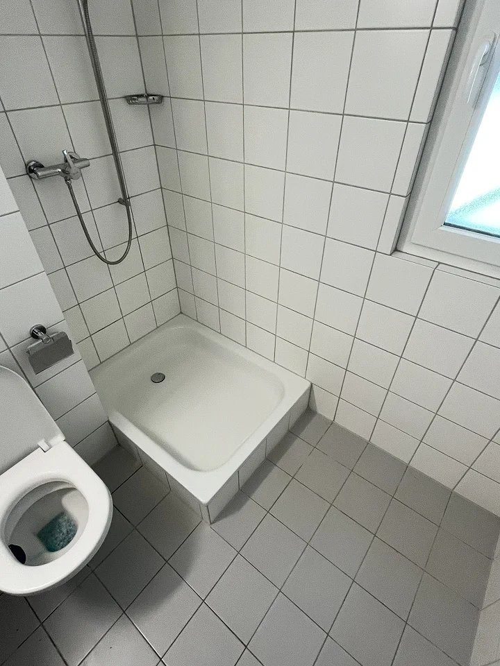Après travaux de la même salle de bain, montrant un espace propre et rafraîchi. Sol carrelé en gris impeccable et douche brillante.